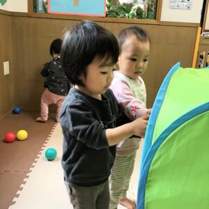 室内遊びのトンネルを先生が組み立て中です。お友だちは早く遊びたいと待てない様子です。