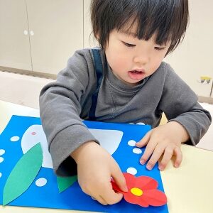 赤い花を貼り製作を完成させる子ども