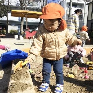 スコップで砂場の砂を盛る子ども