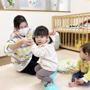 平均台に乗り足の裏で凹凸を確かめる子どもと支える先生