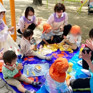 公園でシートを敷いてお弁当を食べる子どもたちと保育士