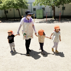 手を繋いで歩く保育士と子どもたち