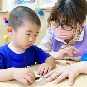 保育士に手伝ってもらいながらお父さんの顔を製作する子ども