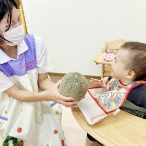 保育士が持つ大きなメロンを前に微笑む子ども