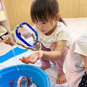 ペットボトルで作った容器ですくった水を触る子ども