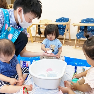 たらいを囲んで水遊びをする子どもたちと保育士