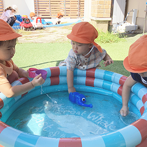 輪になってプールにはった水に触れる子どもたち