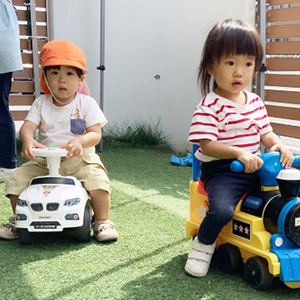 園庭で車に乗って遊ぶ子どもたち