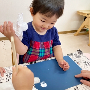 はにかみながら布につけた白い絵の具を画用紙につける子ども