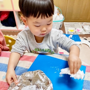 ティッシュペーパーに付けた白い絵の具で青い画用紙に色を着ける子ども