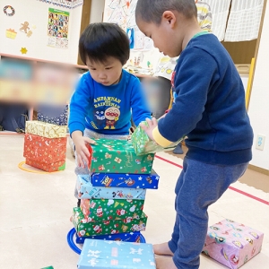 クリスマスプレゼントに見立てた箱を高く積むゲームをする子どもたち