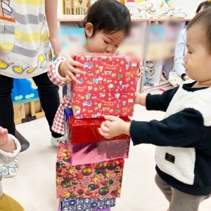 クリスマスプレゼントに見立てた箱を高く積むゲームをする子どもたち