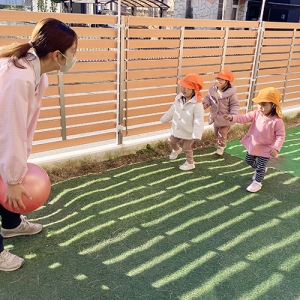 園庭でボール遊びをする子どもたちと保育士