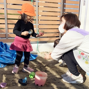 砂場で作ったケーキを保育士に渡す子ども