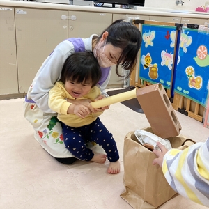 先生に支えられながら手作りの杵と臼でお餅つきをする子ども