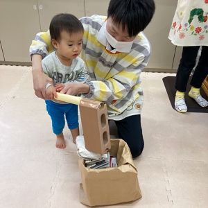 先生に支えられながら手作りの杵と臼でお餅つきをする子ども