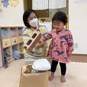 先生と一緒に手作りの杵と臼でお餅つきをする子ども