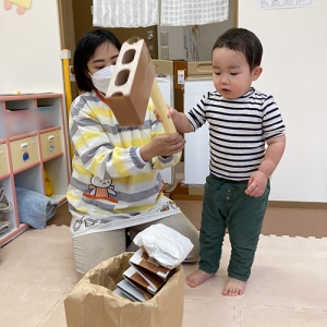 先生と一緒に手作りの杵と臼でお餅つきをする子ども