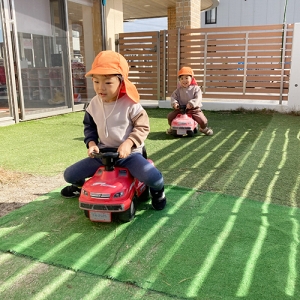 車のおもちゃに乗って競争をする子どもたち