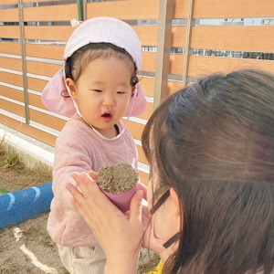 砂場で作ったものを先生に「どうぞ」する子ども