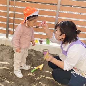 砂場で先生と一緒に食べる真似をする子ども