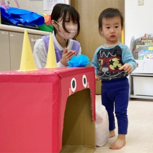 箱の赤鬼の頭にカラフルな髪の毛を貼り付ける子ども