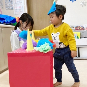 箱の赤鬼の頭にカラフルな髪の毛を貼り付ける子ども