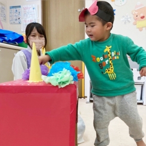 箱の赤鬼の頭にカラフルな髪の毛を貼り付ける子ども