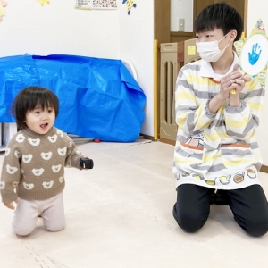 手にミニカーを持って笑顔を見せる子どもと見守る保育士