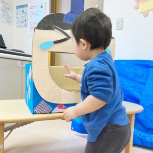 大きな口を開けたお内裏様にボールのあられを入れる子ども