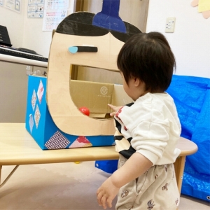 大きな口を開けたお内裏様にボールのあられを入れる子ども