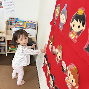 壁面のひな壇にひな人形を飾って笑顔を見せる子ども