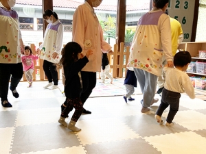 曲に合わせ保育士と手をつないでダンスをする子どもたち