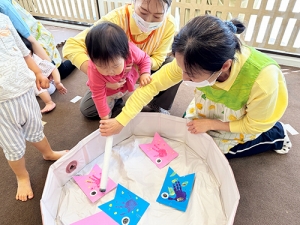保育士に手を取ってもらいながら鯉のぼり釣りをする子ども