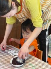 ピンを入れる箱にスタンプで飾り付けする子どもとサポートする保育士