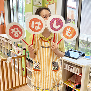 「おなしも」のプレートを持って子どもたちに話をする保育士