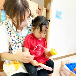 保育士の膝に座り、紙製のアイスクリームを手に持つ子ども