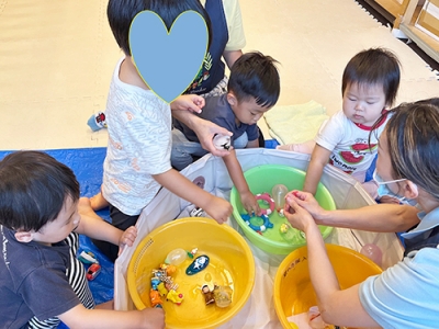 たらいの周りに集まりおもちゃが閉じ込められた氷を触る子どもたち