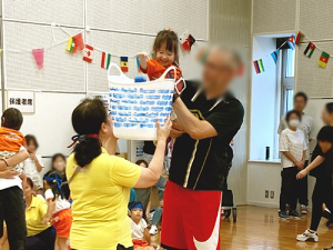 保護者に抱き上げられてカゴに玉を入れる子ども