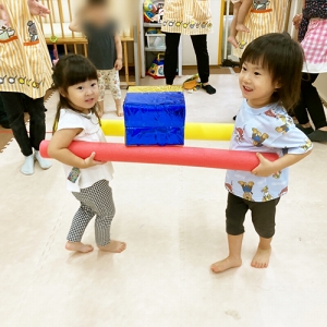 お友だちと協力して2本の棒に乗せた荷物を運ぶ子ども