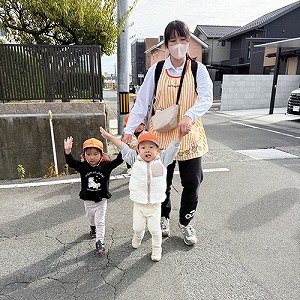 手をあげて道を横断する保育士と子どもたち