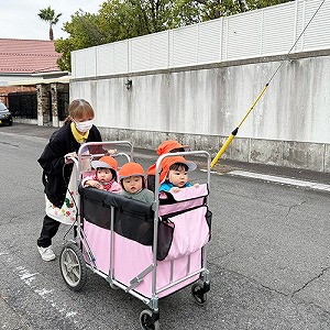 お散歩カーに乗って先生と散歩にでかける子どもたち