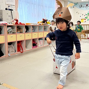 トナカイのお面を被り、ソリを引いて走る子ども