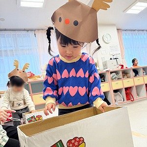 トナカイのお面を被り、ツリーに飾るオーナメントを選ぶ子ども