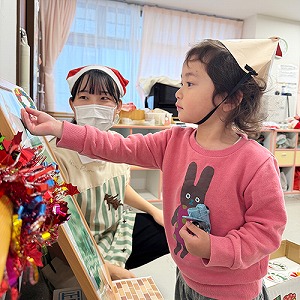 トナカイのお面を被り、オーナメントをツリーに飾る子ども