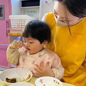 スプーンでスープを飲む子どもと、子どもを支える先生