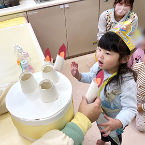 お友だちが飾り付けしたケーキのロウソクの火を吹き消す子ども