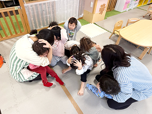 地震発生を想定した訓練で頭を守る保育士と子どもたち