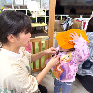 保育士に防災用の帽子を被せてもらう子ども