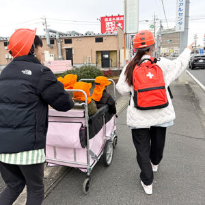 避難訓練で子どもたちを乗せたお散歩カートを押しながら歩道を歩く保育士たち